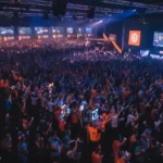 Una multitud animando en el evento de juego de QuakeCon entre pantallas que muestran juegos y logotipos de id Software.